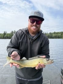 An angler proudly displaying a Walleye caught during a fishing trip on a serene lake, showcasing the excitement of freshwater fishing.