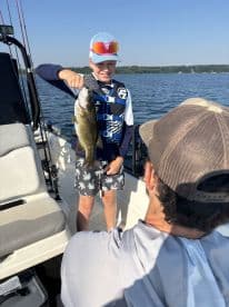 A young angler proudly displaying a large Bass while fishing on a boat, showcasing a fun day on the water.