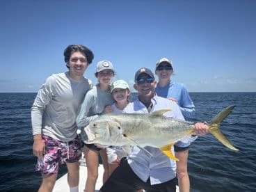 A family proudly displays a large Jack Crevalle caught during a fishing trip on a sunny day.