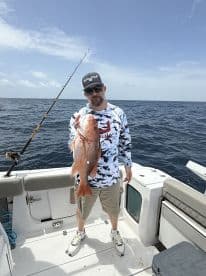 Angler proudly displaying a large Red Snapper while fishing offshore, showcasing a successful day on the water.