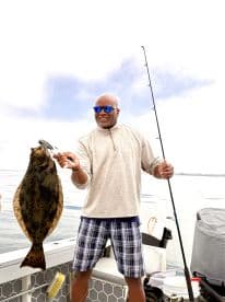 An angler proudly displaying a large Flounder while fishing on a boat, showcasing a successful day on the water.