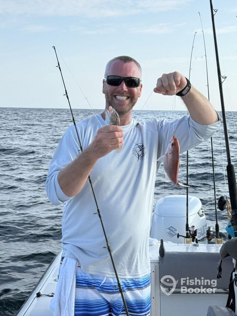 An enthusiastic angler proudly displaying his catch of a Snapper and a small fish while fishing offshore.
