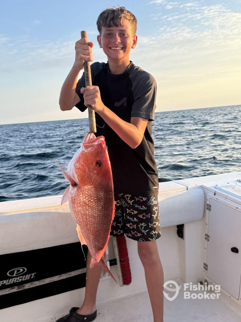 Young angler proudly holding a large Red Snapper while fishing on a boat, showcasing a successful catch during a sunny day at sea.