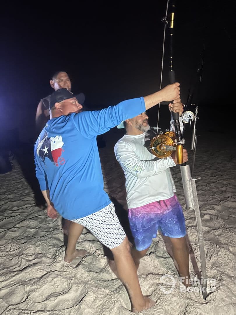 Anglers engaged in a night fishing adventure, working together to reel in a catch on the sandy beach.