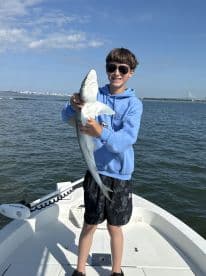 Young angler proudly holding a small shark while fishing on a boat, showcasing a successful catch in a coastal environment.