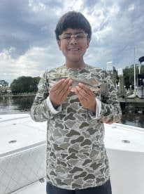 Young angler proudly holding a small fish while standing on a boat, showcasing a successful fishing trip.