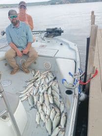 A couple relaxing on a boat with a large catch of striped bass laid out on the deck after a successful fishing trip.