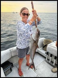 An angler proudly displaying a large fish while fishing on a boat during a sunset.