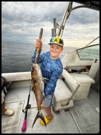 A young angler proudly displaying a large fish aboard a fishing boat, showcasing a successful day on the water.