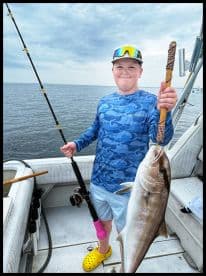 A young angler proudly displaying a large fish aboard a boat, showcasing a successful fishing trip.
