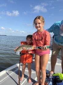 Two young girls proudly displaying a caught fish while enjoying a day of fishing on a boat.
