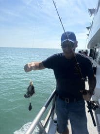 An angler proudly displaying a freshly caught fish while fishing off the coast, with a beautiful ocean backdrop.