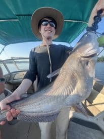 An angler proudly displaying a large Catfish while on a boat, showcasing a successful fishing trip.