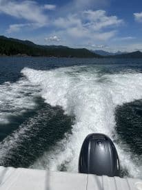 A scenic view from the back of a boat cruising through calm waters, surrounded by lush green mountains and a clear blue sky.