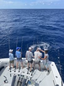 A group of young anglers actively reeling in a fish while fishing on a charter boat in deep blue waters.