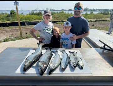 A family proudly displays their catch of six Salmon on a board at a scenic fishing location.