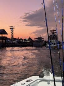 A scenic view of a boat navigating through the harbor at sunset, showcasing the vibrant colors of the sky and the silhouettes of nearby structures.