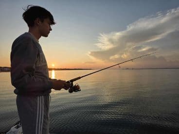 A young angler casting a line into calm waters during sunset, creating a serene fishing atmosphere.