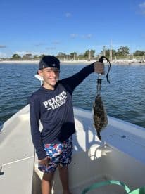 A young angler proudly displaying a Flounder while fishing from a boat in a scenic coastal environment.