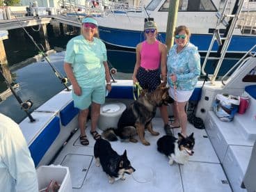 A group of women and their dogs enjoying a day on a fishing boat, showcasing a relaxed atmosphere with seating and fishing gear visible.