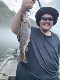 Angler proudly displaying a vibrant Rainbow Trout while fishing from a boat, surrounded by a scenic misty backdrop.