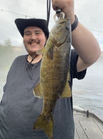 Happy angler displaying a freshly caught Smallmouth Bass while fishing from a boat.