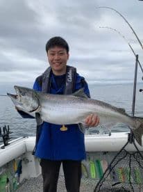 An angler proudly displaying a large Chinook Salmon aboard a fishing boat in a scenic marine environment.