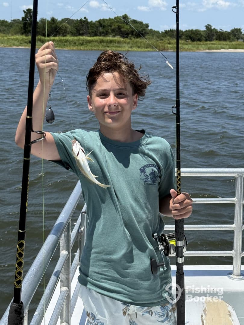 A young angler proudly holding a small fish while fishing on a boat in a scenic waterway.