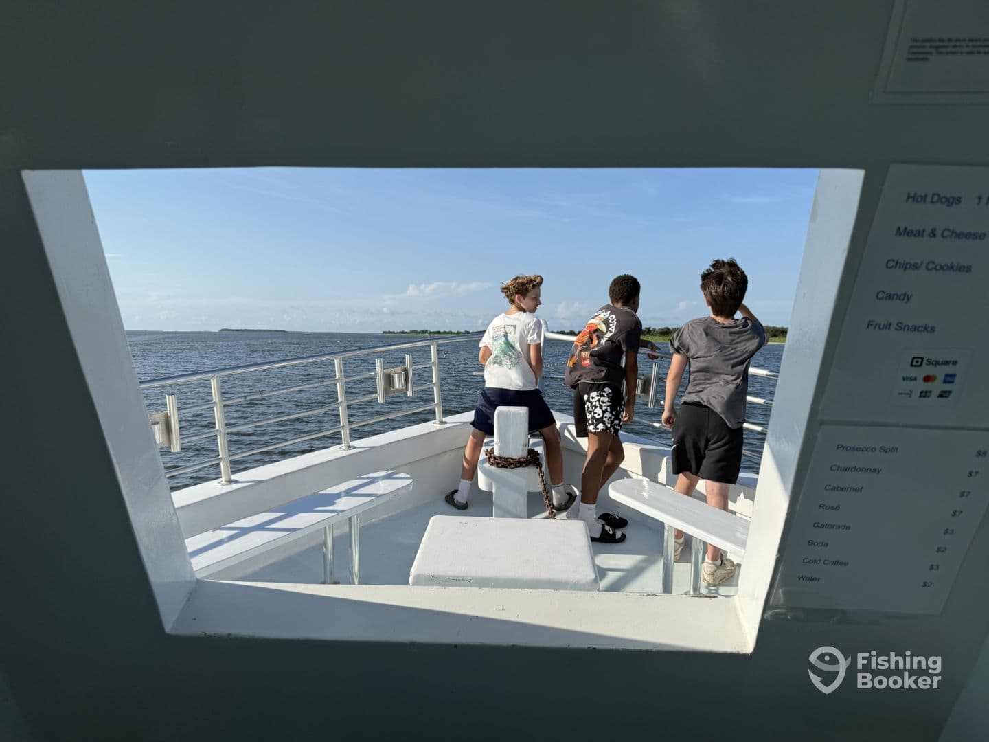 A group of young anglers enjoying the view from the interior of a fishing boat, with a menu visible on the wall, showcasing a variety of snacks and beverages.