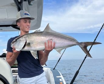 Young angler proudly displaying a large Amberjack while fishing offshore, showcasing a successful day on the water.