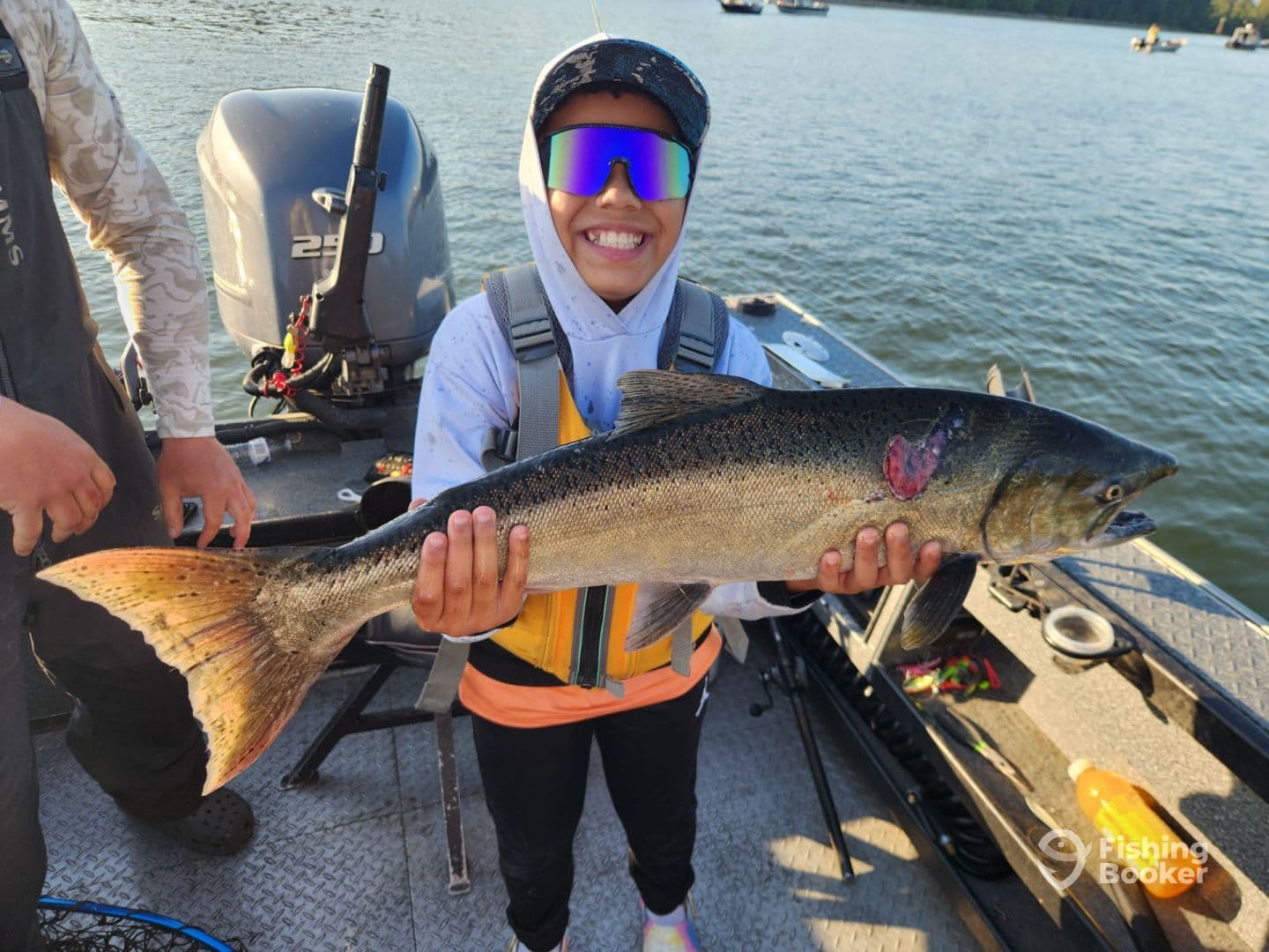 A young angler proudly displaying a large trout while fishing on a boat, showcasing a successful day on the water.