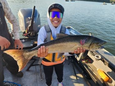 A young angler proudly displaying a large trout while fishing on a boat, showcasing a successful day on the water.
