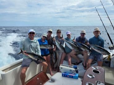 A group of anglers proudly displaying their catch of Yellowfin Tuna aboard a sportfishing boat in open waters.