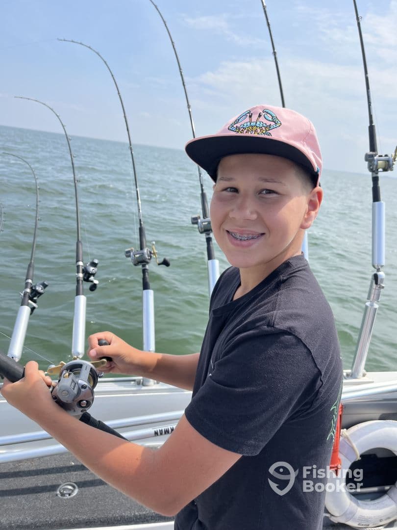 A young angler actively reeling in a fish while fishing on a boat, surrounded by fishing rods and the open water.