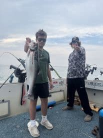 Two young anglers proudly displaying a large Salmon on a fishing boat, showcasing a successful day on the water.