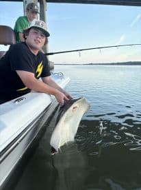 A young angler is reeling in a stingray while fishing from a boat, showcasing an exciting moment on the water.