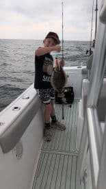 A young angler proudly displaying a caught Flounder while fishing on a boat, showcasing the excitement of a day on the water.