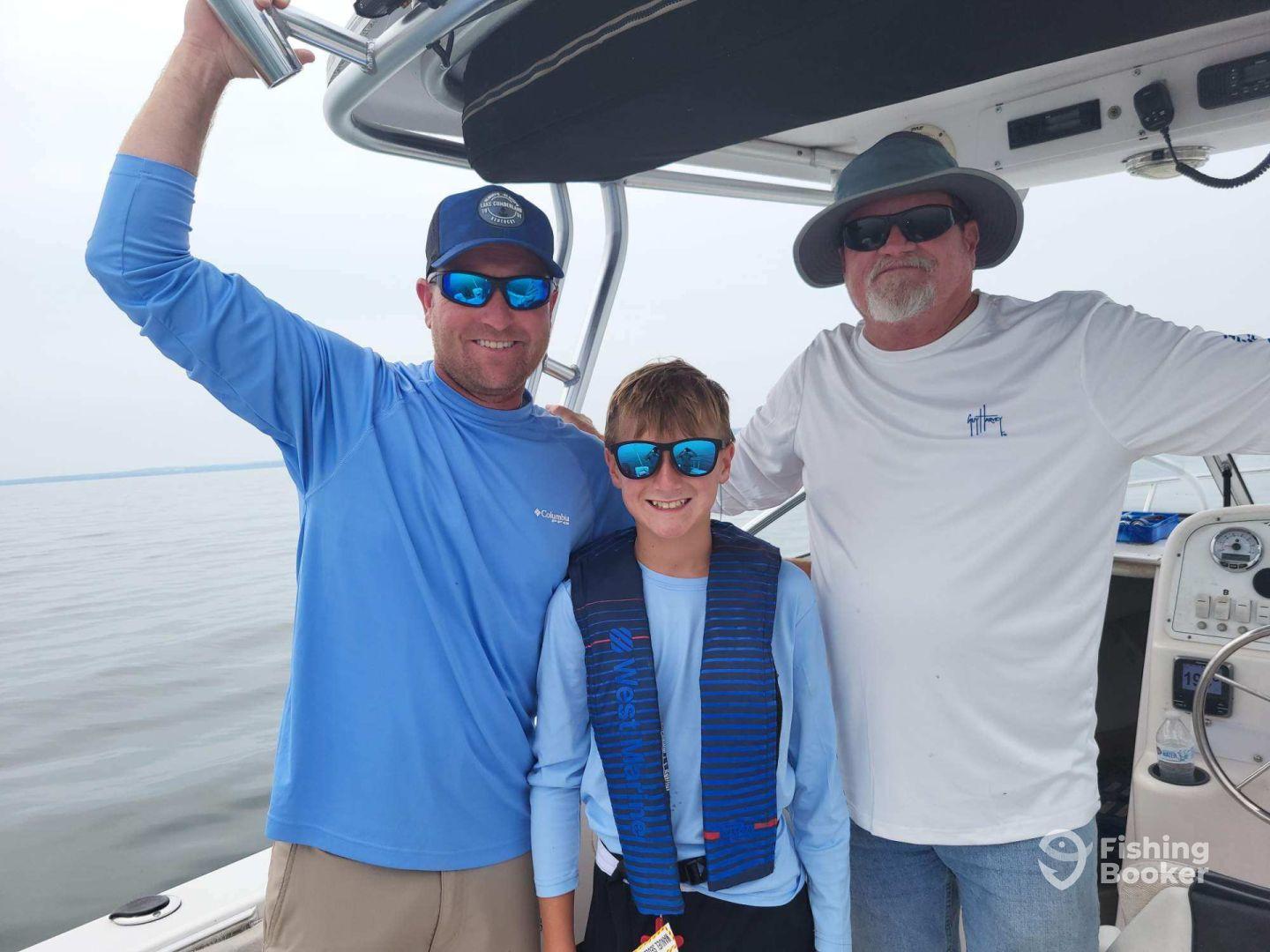 A family enjoying a day on the water, with a young boy in a life jacket smiling between two adults on a fishing boat.