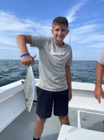 A young angler proudly displaying a Spanish Mackerel while fishing on a boat, showcasing a successful day on the water.
