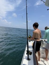 A young angler actively reeling in a fish while fishing on a boat in open water, showcasing the excitement of the sport.