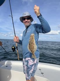 An angler proudly displaying a Flounder while fishing on a boat in open waters.
