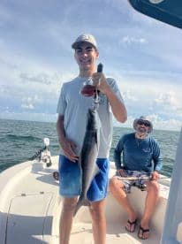A young angler proudly displaying a caught fish while fishing on a boat, with a scenic ocean backdrop.