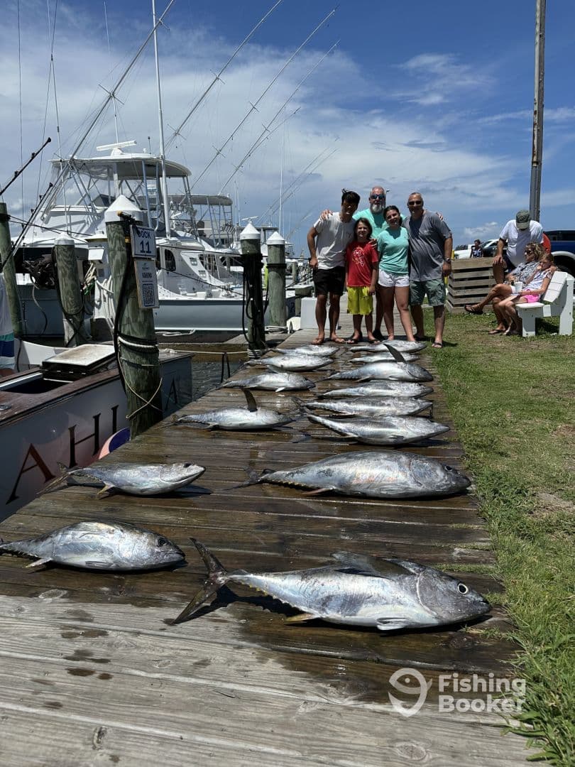 A family poses proudly by a catch of several large Tuna on a dock, showcasing their successful fishing trip.