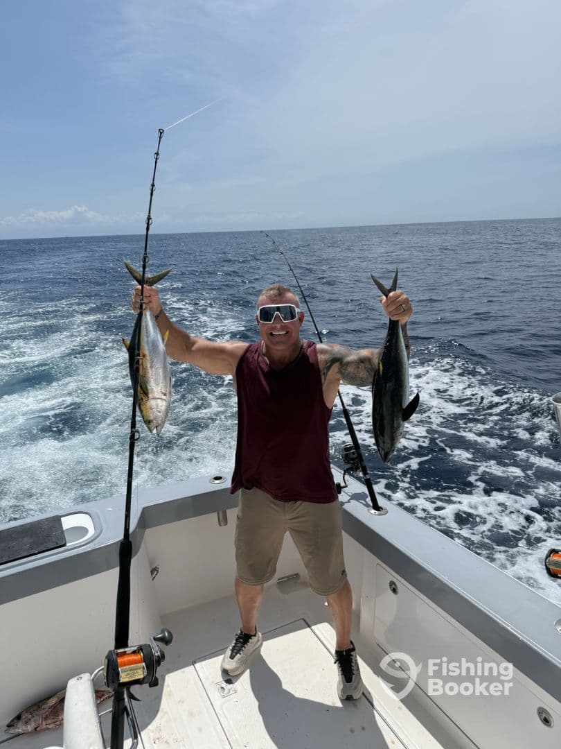 An enthusiastic angler proudly displaying two large fish while aboard a fishing boat in open waters.