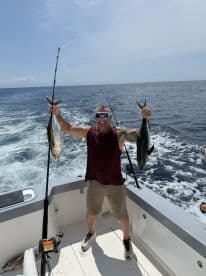 An enthusiastic angler proudly displaying two large fish while aboard a fishing boat in open waters.