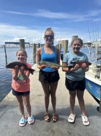 Three young anglers proudly displaying their catches, including a Mahi Mahi and a Snapper, at the dock after a successful fishing trip.