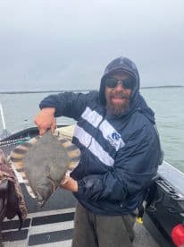 Angler proudly displaying a large Flounder while fishing on a cloudy day.