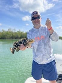 An angler proudly displaying a large Goliath Grouper while fishing in a scenic coastal environment.