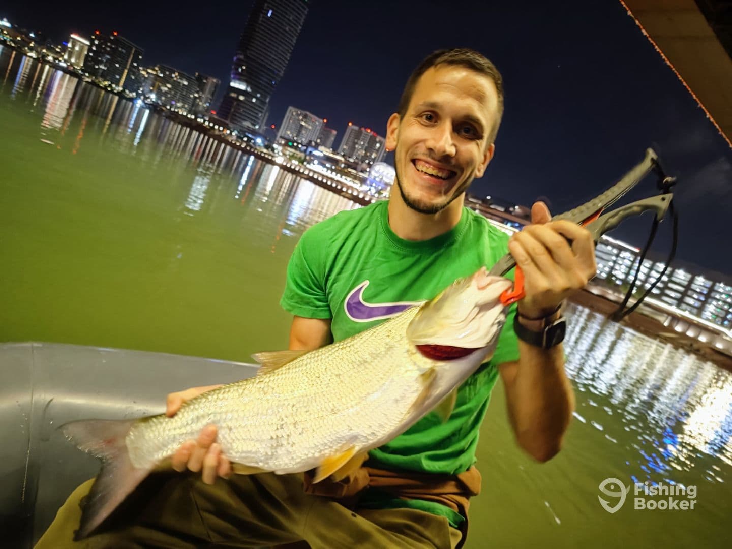 Angler holding a large fish while fishing at night in an urban setting, showcasing a successful catch.