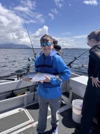 A young angler proudly displaying a caught fish while fishing on a boat, surrounded by a scenic ocean backdrop.